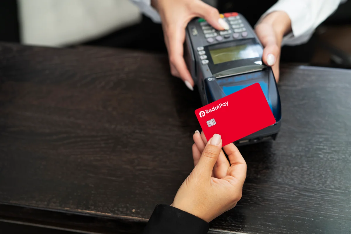 Mano pagando con una tarjeta física roja de RedotPay en un terminal de pago